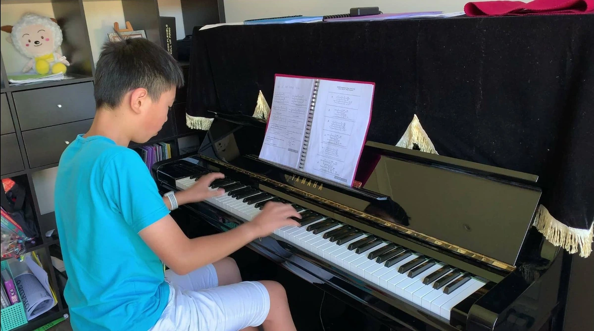 Isaac practising on the used Yamaha U3 upright piano in a blue T-shirt